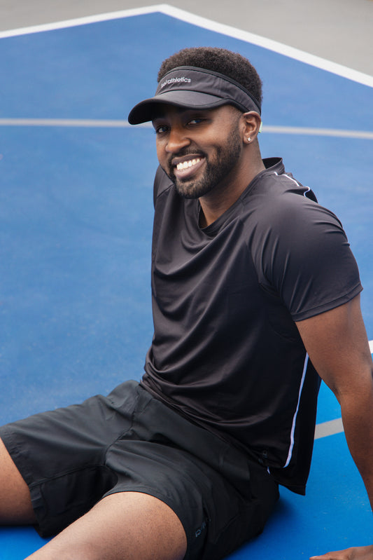 male pickleball player wearing black unlined athletic shorts and a black athletic shirt and black visor on pickleball court