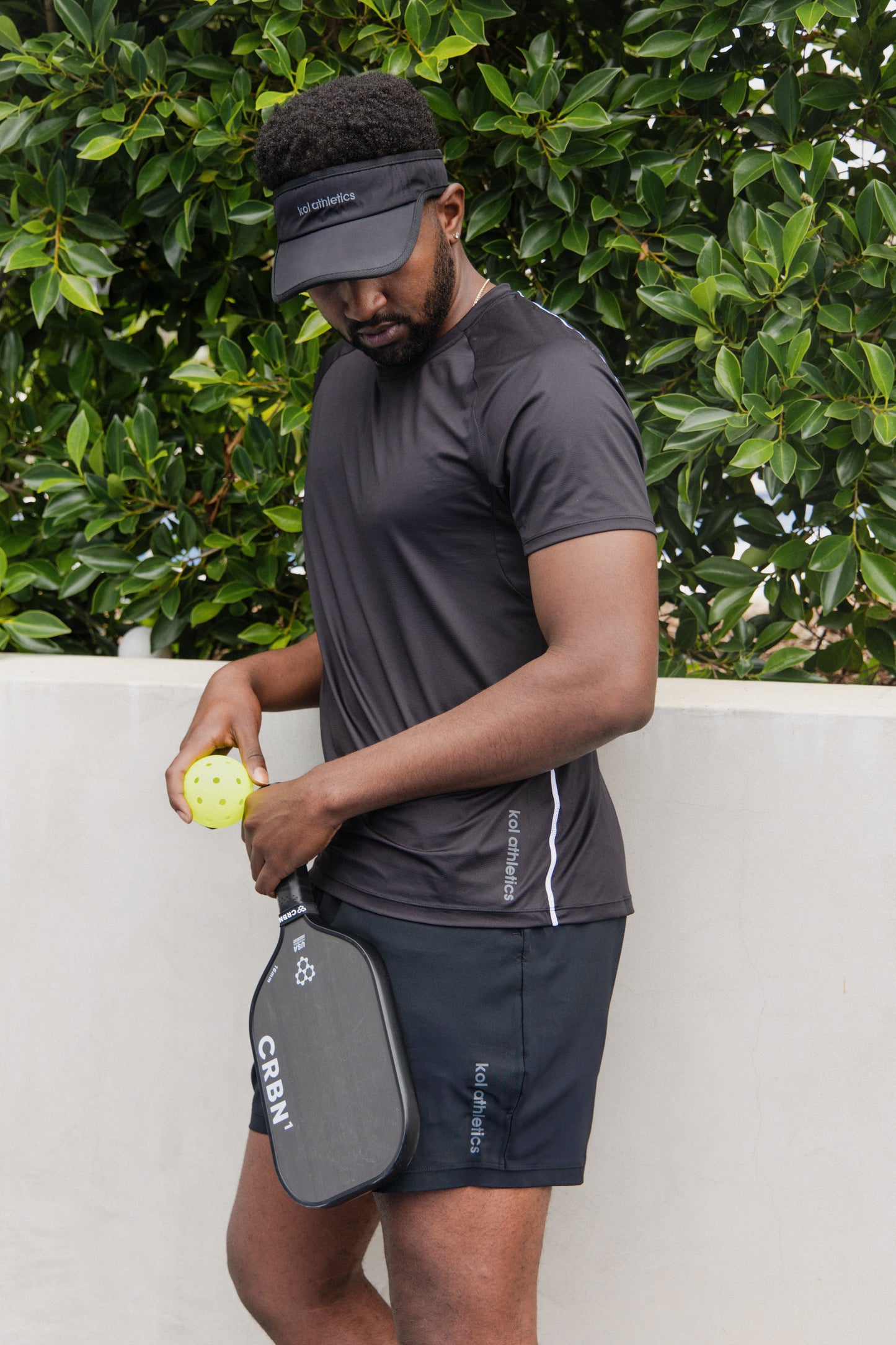 male pickleball player wearing black unlined athletic shorts and a black athletic shirt and a black sweat wicking visor