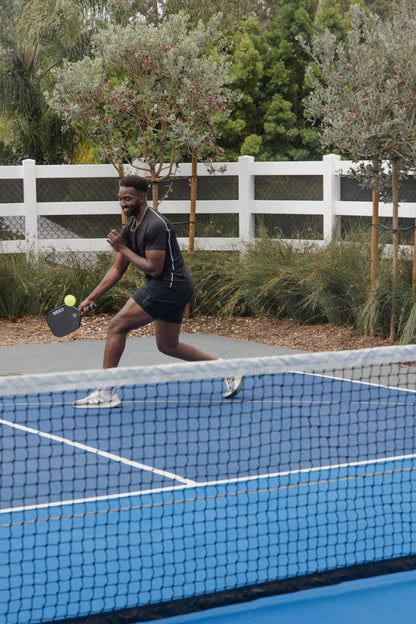 male pickleball player wearing black unlined athletic shorts and a black athletic shirt playing pickleball